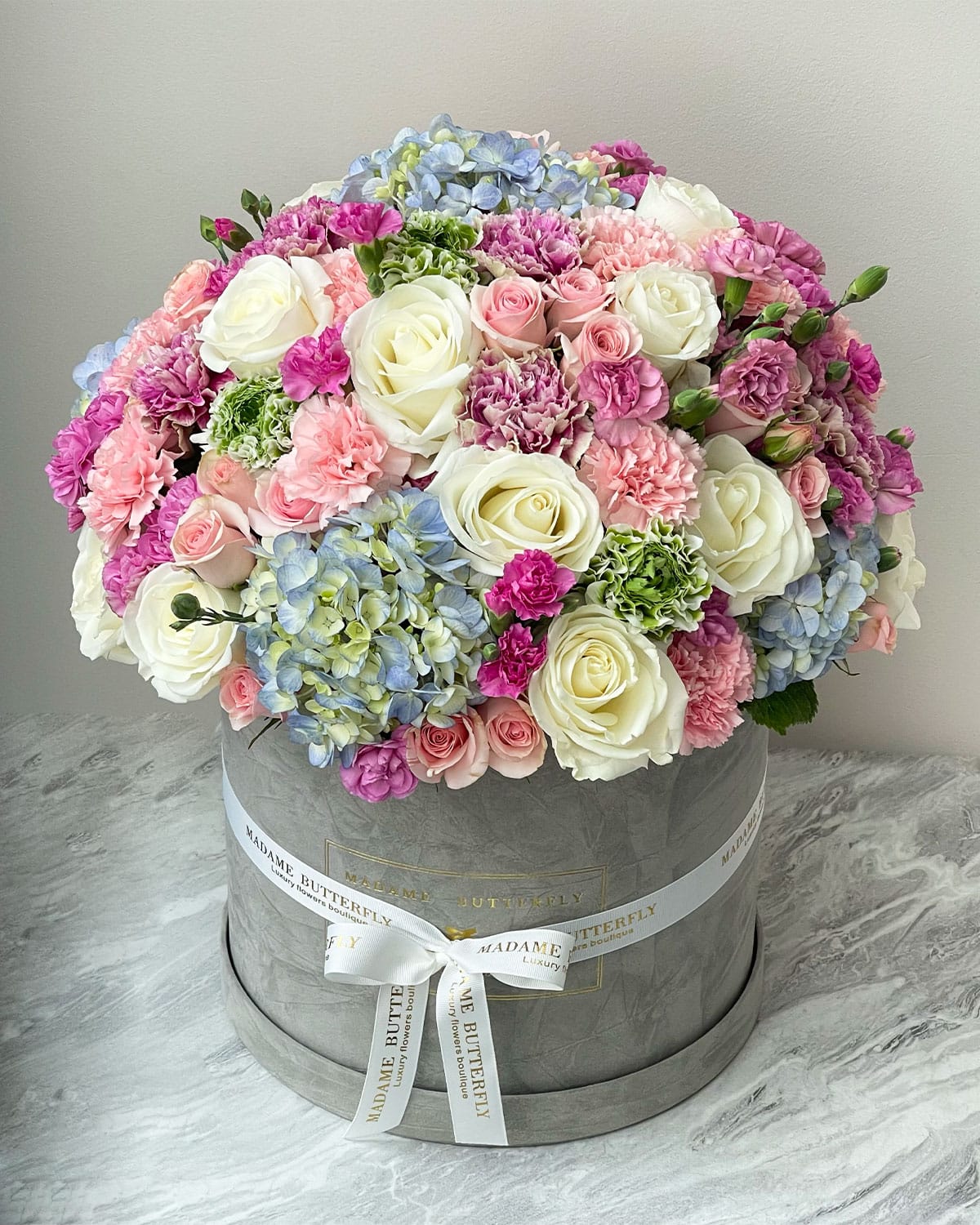 La Dolce Vita es un suspiro envuelto en terciopelo, un gesto que habla con la dulzura de los días felices y la belleza de lo que permanece. Con rosas suaves y hortensias vaporosas, este arreglo acaricia los momentos en los que la sensibilidad merece su propio altar.